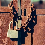 Padlock with shackle and locking mechanism closeup one portable lock on chain on unpainted rusty metal gate doors outdoor on blurred background